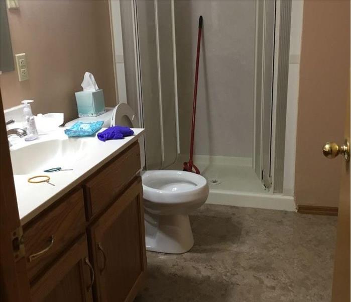 Bathroom with vanity, toilet, and floor damaged with shower in background