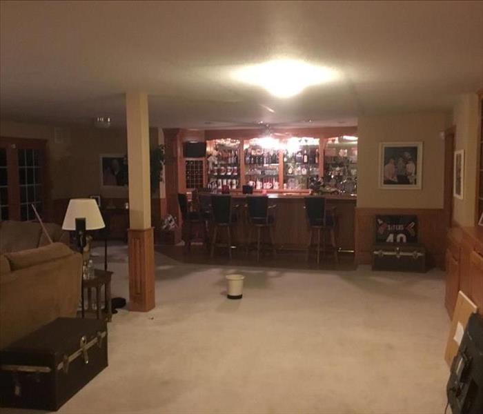 Family room with wet carpet, contents, bucket catching water from ceiling, and bar in the back