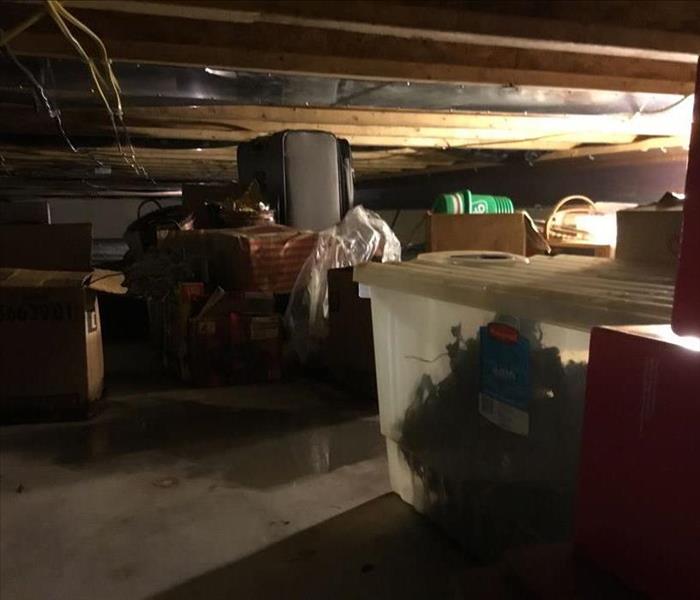 Crawl space full of boxes with water on the floor.
