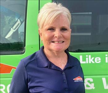 female owner standing in front of a SERVPRO green van.